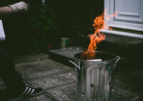 A stainless steel trash can outside with flames and smoke, creating a dramatic scene.